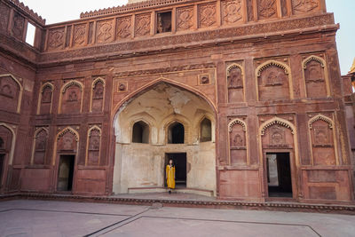 Full body woman in yellow dress standing in arch of aged agra fort in uttar pradesh, india