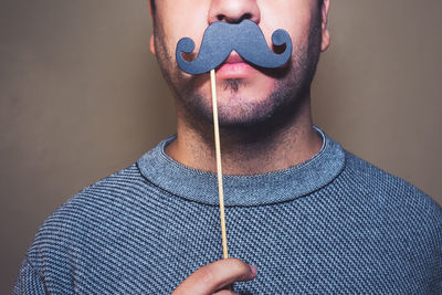 Close-up of man with prop mustache against gray background