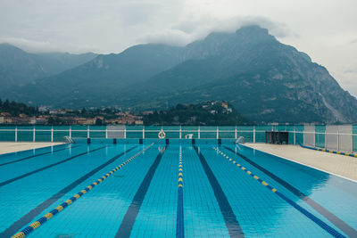 Swimming pool by lake against cloudy sky