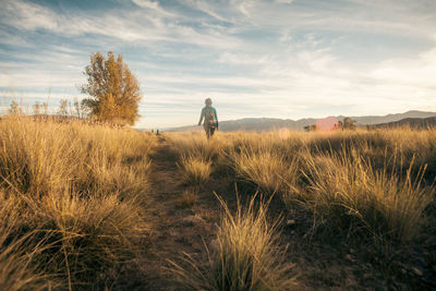 Rear view of woman walking on field against sky