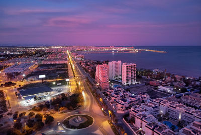 High angle view of illuminated city by buildings at night