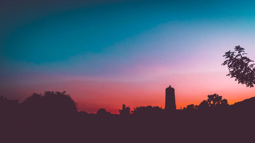 Silhouette trees and buildings against sky at sunset