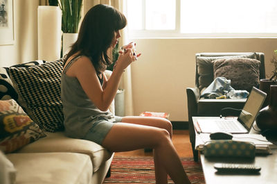 A girl sitting in the couch, drinking coffee, working from home wearing comfortable clothes