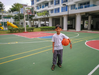 Full length portrait of boy holding basketball at court
