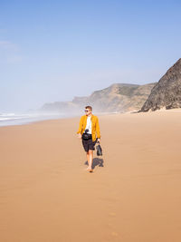Rear view of man walking on sand at beach against sky