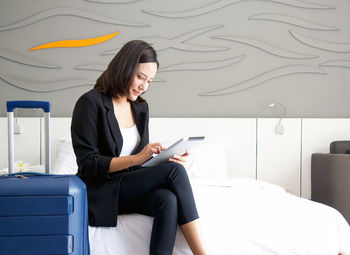 Young woman using mobile phone while sitting on bed