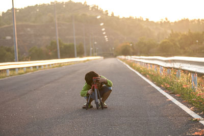 Full length of boy playing with tripod while crouching on road