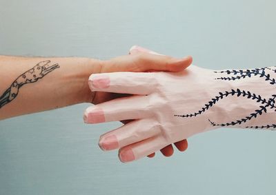 Cropped image of man shaking hands with mannequin against wall