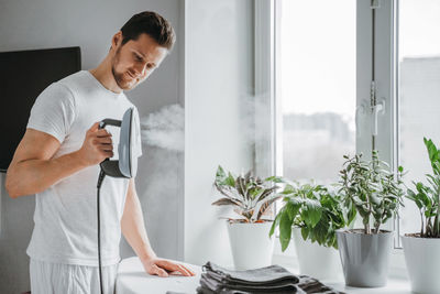 Young man holding camera while standing by window