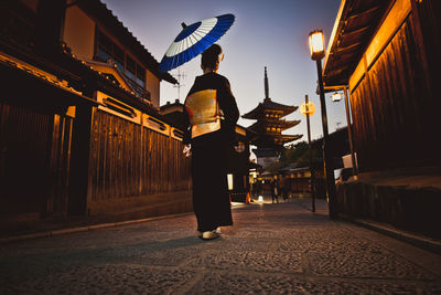 Rear view of man standing on illuminated street amidst buildings in city at night