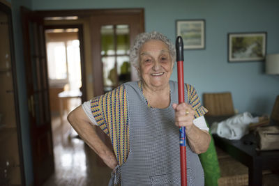 Portrait of smiling senior woman holding stick of cleaning mop