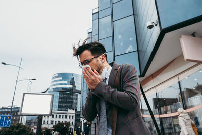 Sick man coughing and sneezing on city street.