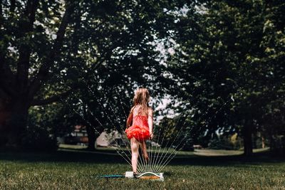 Rear view of girl standing by sprinkler on grass