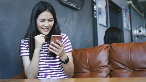 Young woman using smart phone while sitting on laptop