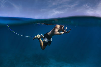Shirtless surfer with surfboard leash swimming undersea at maldives