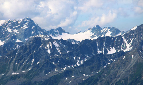 Alpine snow-capped ridges and peaks in the form of a bowl against a sky with clouds