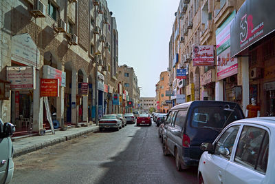 Cars on city street by buildings against sky