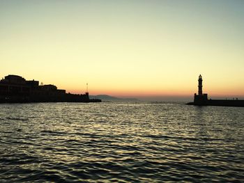 Silhouette buildings by sea against clear sky during sunset