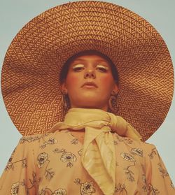 Close-up portrait of a young woman wearing hat against wall