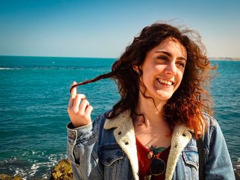 Close-up of smiling young woman standing against sea