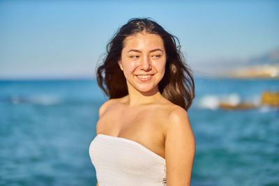 Smiling young woman standing at beach against sky