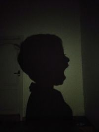 Portrait of silhouette boy standing against wall at home