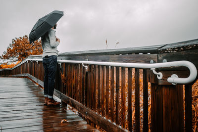 Man standing with umbrella by railing against sky
