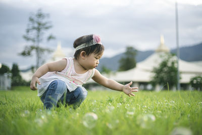 Girl crouching on grass against sky