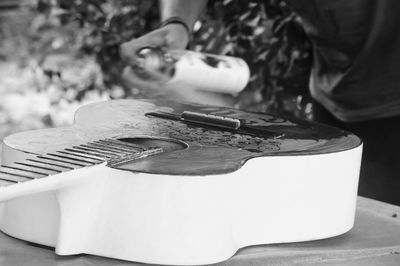 Midsection of man spraying liquid on guitar at table