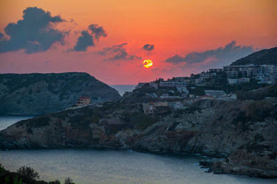 Buildings by sea against orange sky