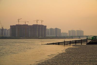 Sea by city against sky at sunset