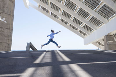 Woman with ponytail jumping in joy and raising arms in urban outside