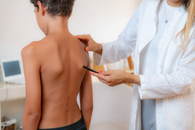 Pediatric doctor examining posture of a boy, making marks on his back, checking angle of scapula