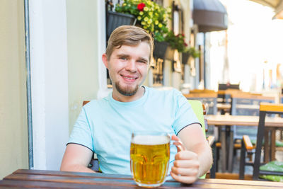 Portrait of young man with drink on table at restaurant