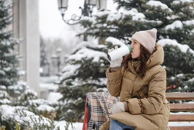 Cheerfully brunette woman drinking from flask outdoors in the city in winter. warming up, enjoying