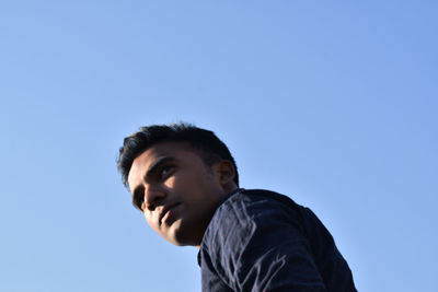 Portrait of young man looking away against clear sky