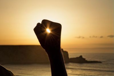 Close-up of silhouette hand against sea during sunset