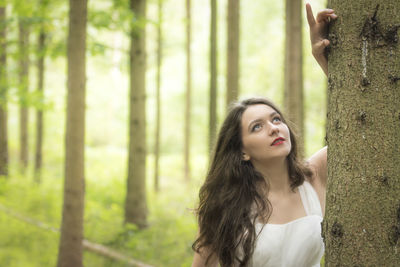 Close-up of young woman standing by tree trunk in forest