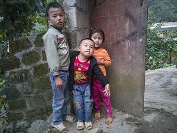 Full length portrait of siblings standing against wall