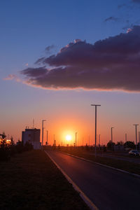 Road by silhouette city against sky during sunset