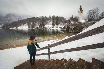 Rear view full length of woman standing by lake on steps during winter