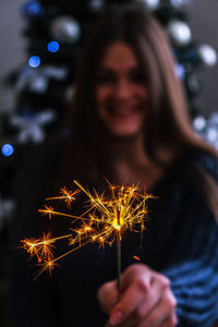 Happy young woman sitting with glass of champagne and bengal light next to the christmas 