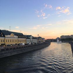 River by buildings against sky during sunset