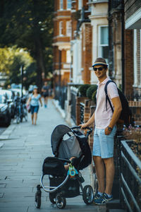 Man with baby carriage standing on street in city