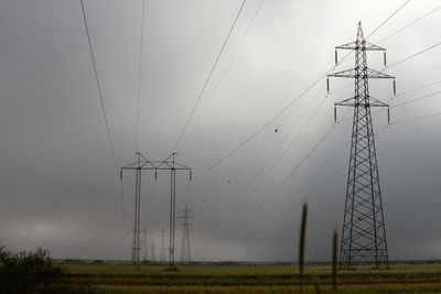 Low angle view of electricity pylon on field against sky