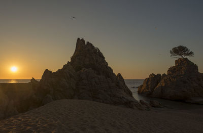 Rocks on beach against sky during sunset