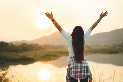 Rear view of woman standing against sky during sunset