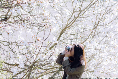 Low angle view of woman standing against bare tree