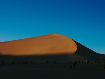 People on desert against clear blue sky