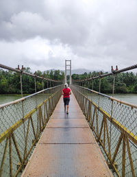 Rear view of man walking on footbridge against sky
